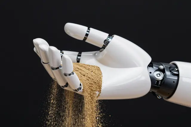A white robotic prosthetic hand releases golden sand that falls between its fingers against a solid black background
