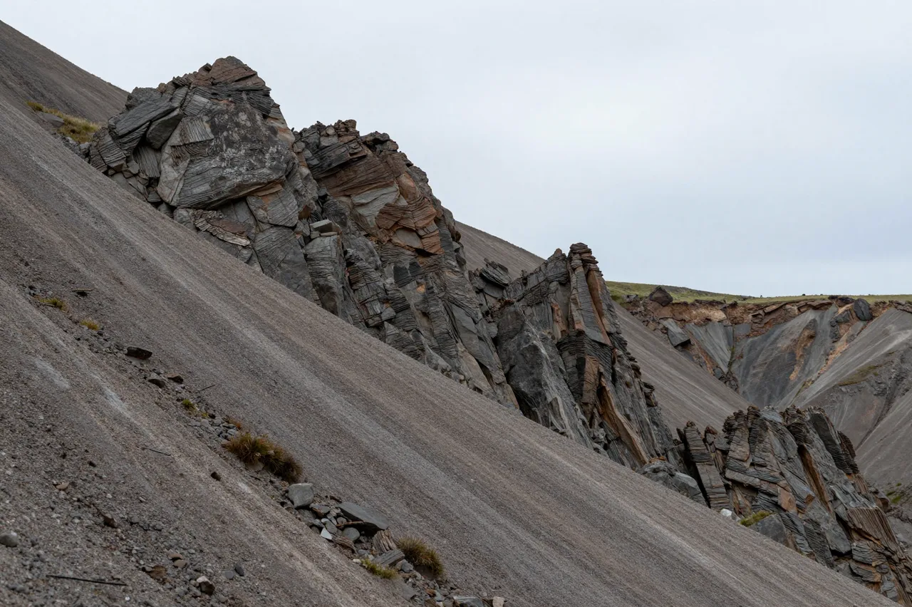 Layered rocky pinnacles rise from gravel scree under a soft overcast sky