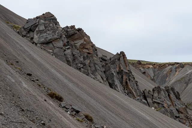 Layered rocky pinnacles rise from gravel scree under a soft overcast sky