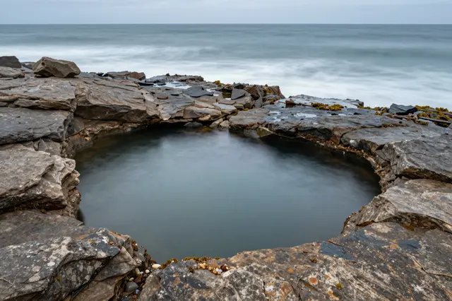 Long exposure view of a calm natural rock pool set into coastal rocks beside the ocean