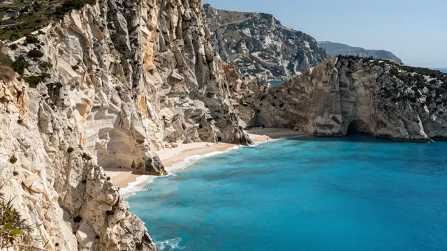 Towering eroded white limestone cliffs frame a secluded sandy cove with bright turquoise sea on a sunny day