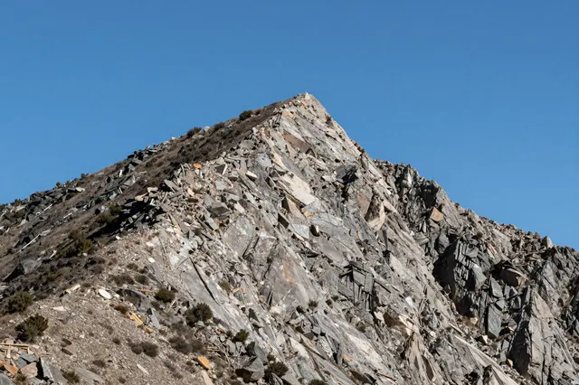 Sharp rocky mountain ridge with sparse desert shrubs rises under a bright clear blue sky