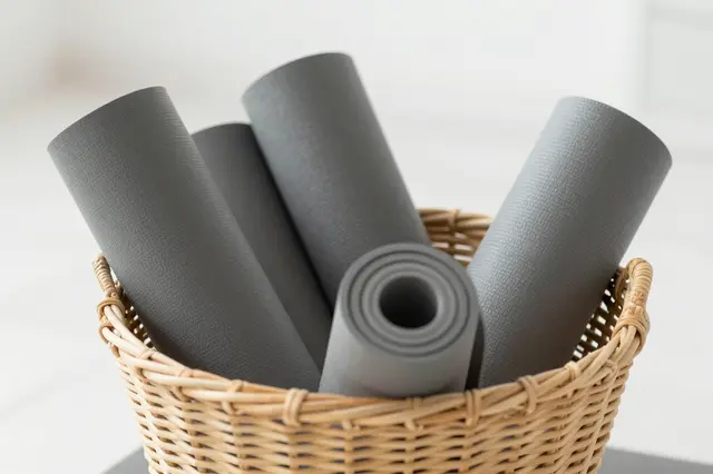 Gray rolled yoga mats sit arranged inside a woven wicker basket in a bright minimal studio.