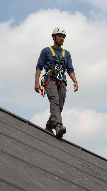 Low angle view of a mixed race roofer in safety gear walking along a roof ridge under a cloudy sky