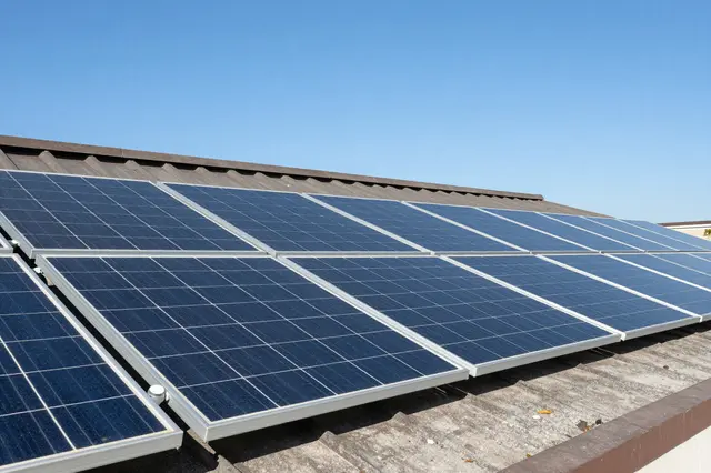 Rows of solar photovoltaic panels mounted on a residential roof beneath a clear bright blue sky