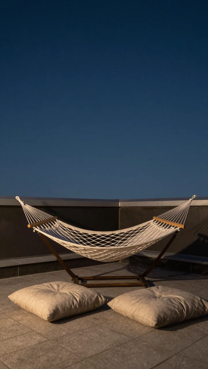 A white mesh hammock sits with two floor cushions on a tiled rooftop under a dark evening sky