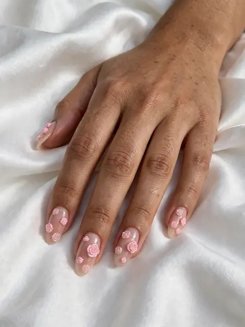 Close-up of a woman's hand with 3D rose almond nail art resting on soft white silk fabric.