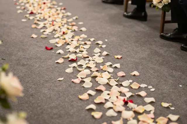 Scattered blush, white and red rose petals line a gray carpeted wedding aisle beside guest seating.