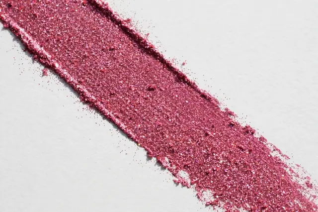 Wide diagonal rose pink glitter brushstroke runs across a matte white surface