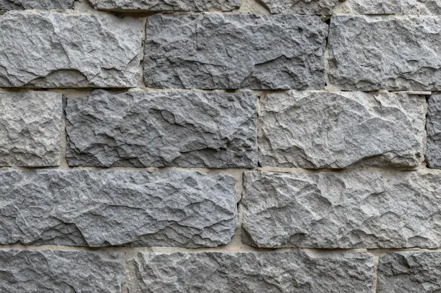 Close up view of rough chiseled gray stone blocks set in light mortar to form a wall surface