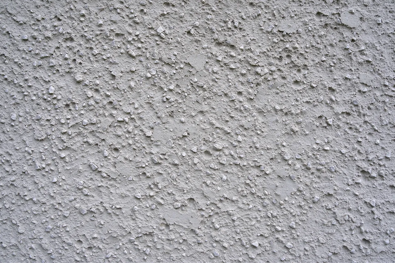 Full frame close-up of pale gray pebbly dash stucco render surface with rough grainy peaks