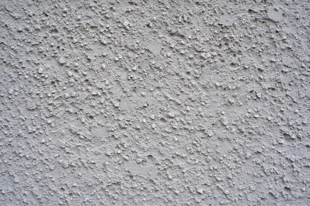 Full frame close-up of pale gray pebbly dash stucco render surface with rough grainy peaks