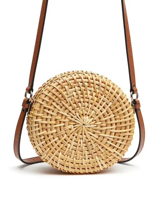 Woven round rattan crossbody bag with leather strap displayed on a plain white studio background