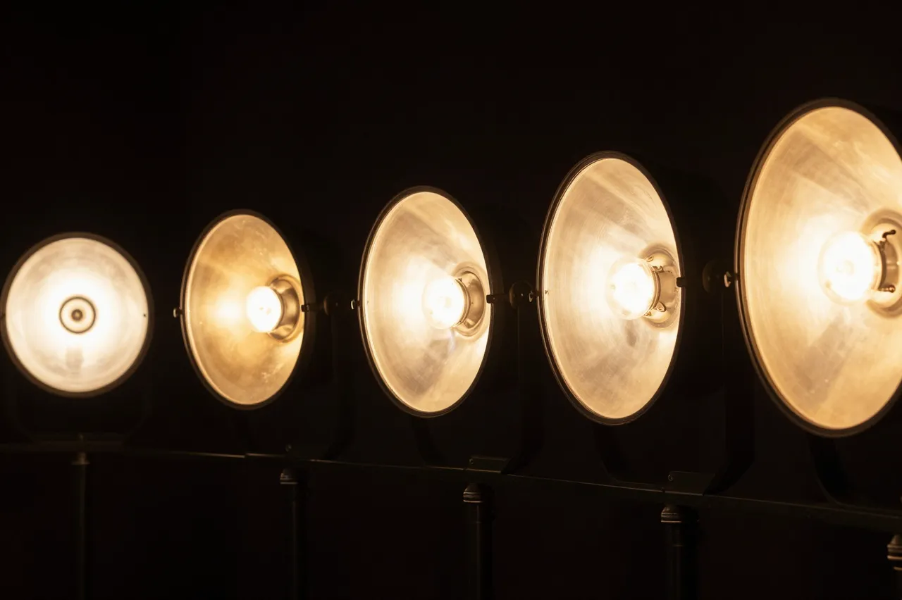A horizontal row of warm amber stage lights glows against a solid black backdrop