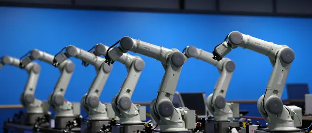 A row of light gray industrial robotic arms arranged in a line against a bright blue wall