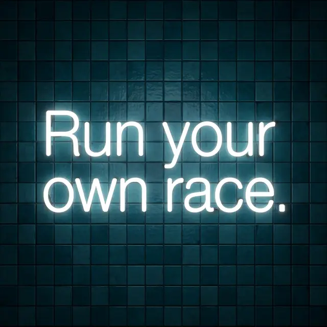 Glowing white neon sign reading "Run your own race." mounted on a dark teal tiled wall