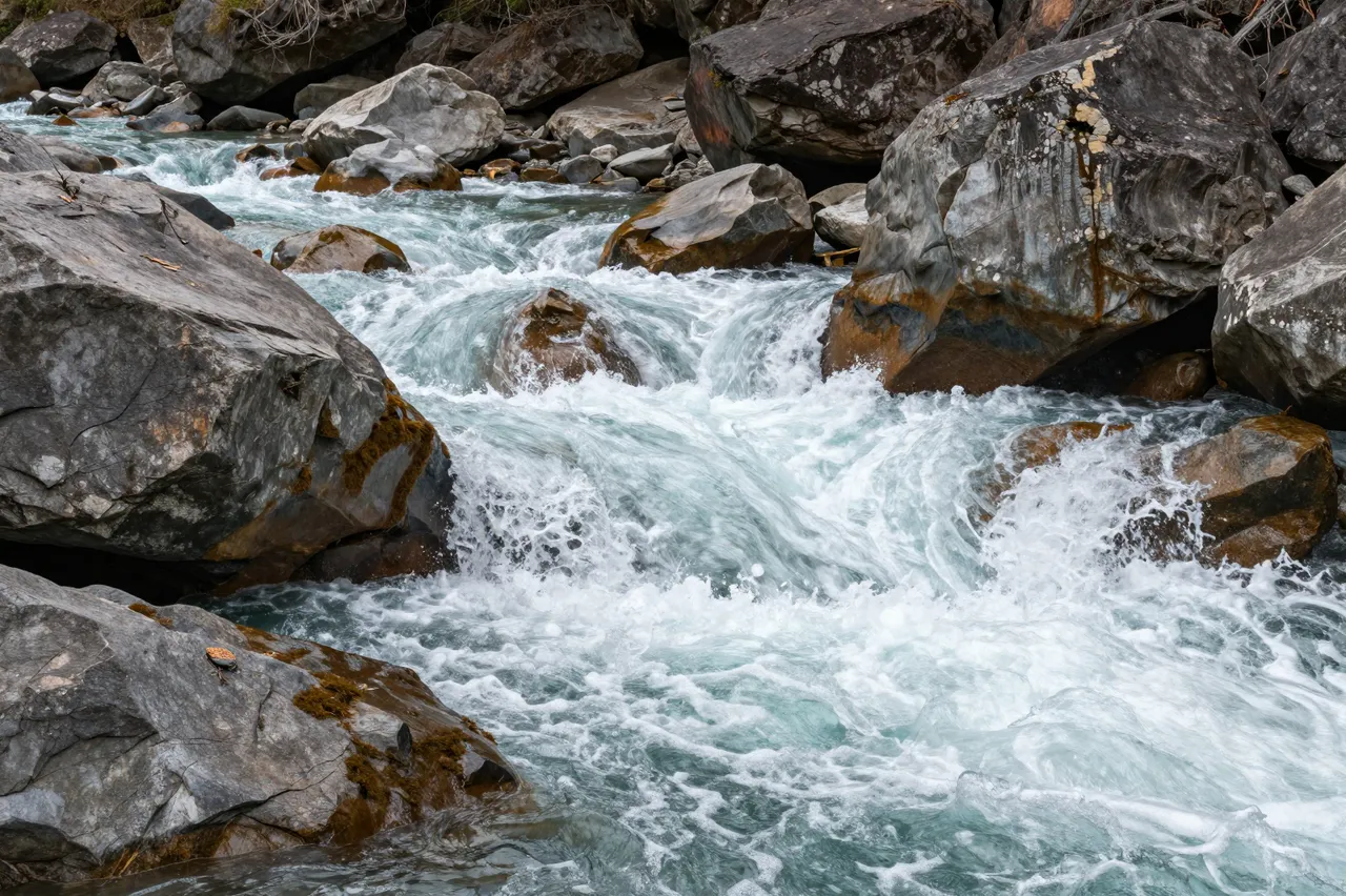 Turbulent turquoise river rapids cascade over large weathered gray boulders in a rocky gorge