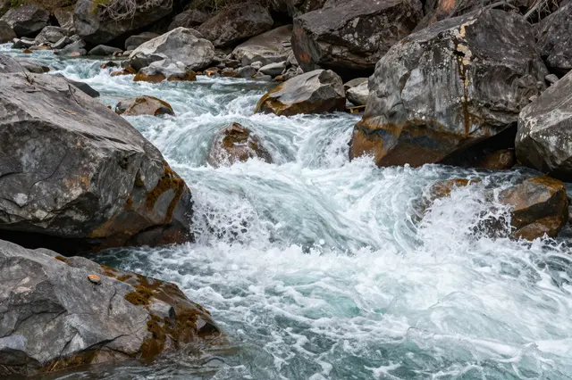 Turbulent turquoise river rapids cascade over large weathered gray boulders in a rocky gorge