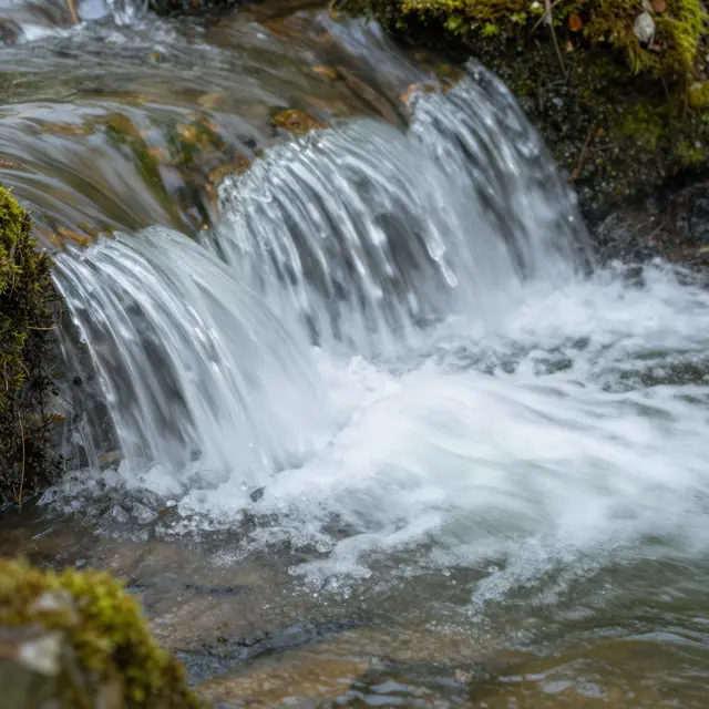 Long exposure close-up of silky flowing water cascading over a moss-covered rocky stream ledge