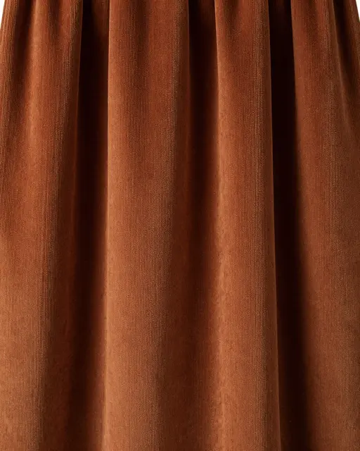 Full frame close-up of draped wide-wale rust corduroy lit by soft side lighting