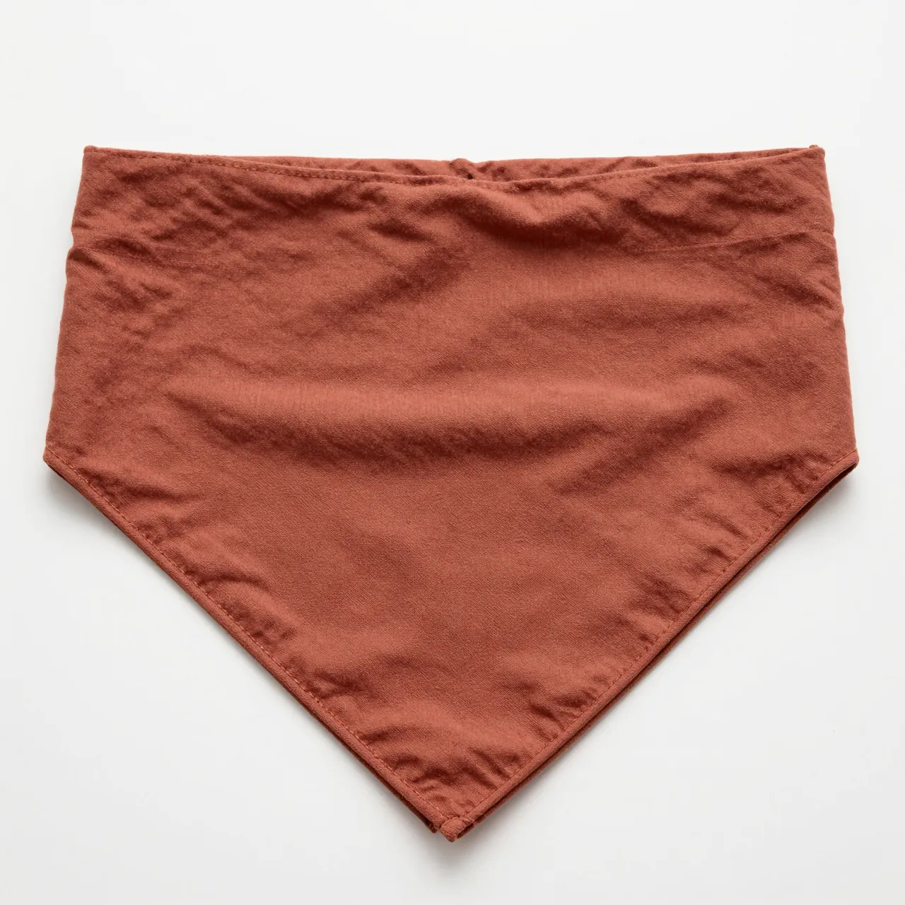 A folded rust brown cotton bandana lies flat on a plain white surface.