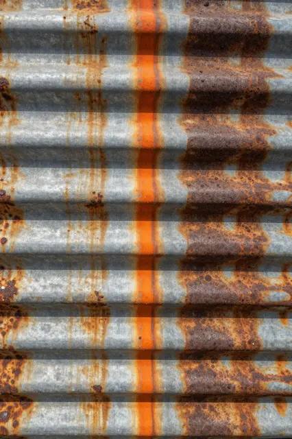 Close-up of weathered corrugated galvanized iron with orange rust drip streaks and dark corroded patches