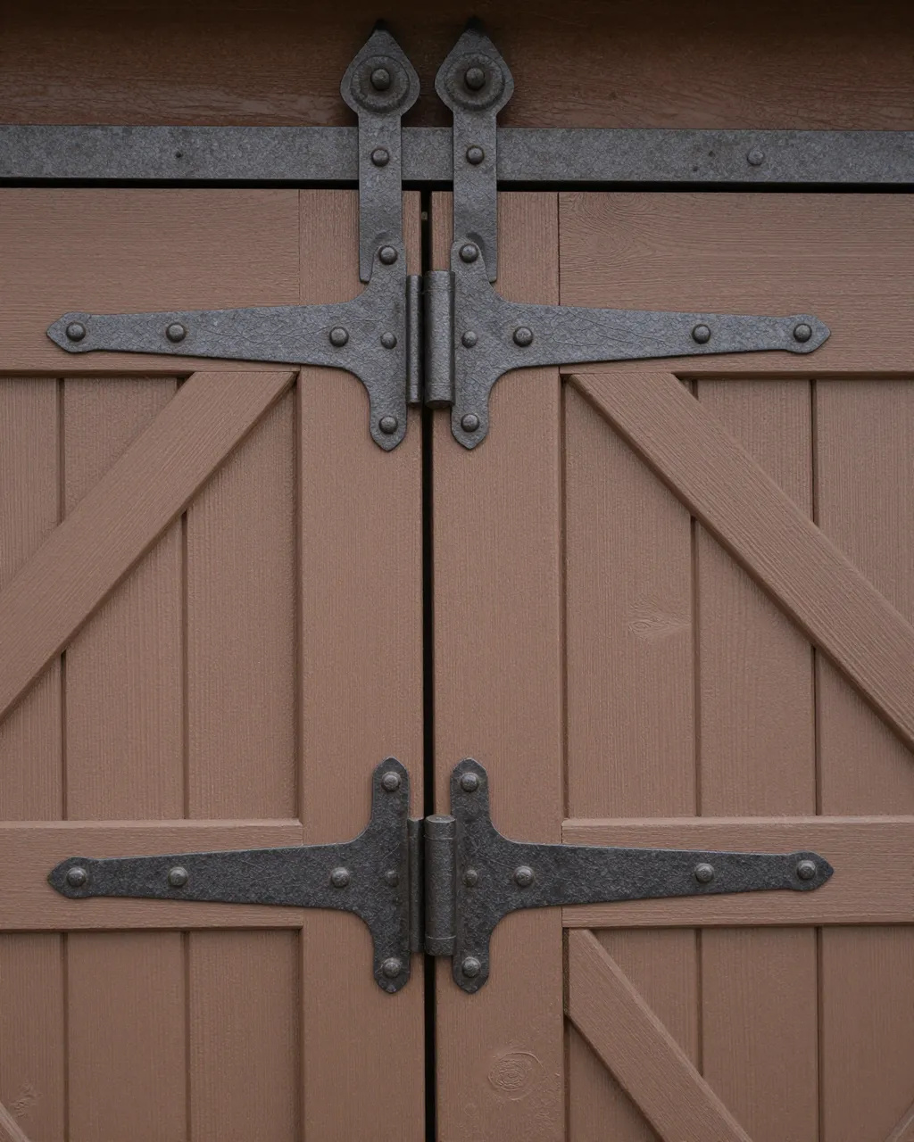 Close-up view of a painted wooden barn door fitted with decorative dark iron hinges and rivets