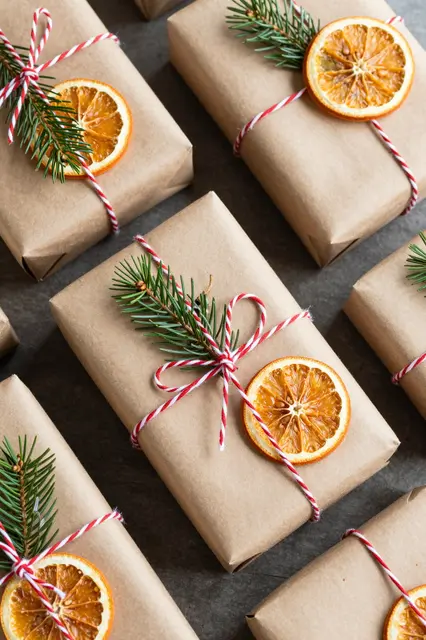 Top view of kraft paper wrapped Christmas parcels decorated with baker's twine, dried orange slices and fir sprigs