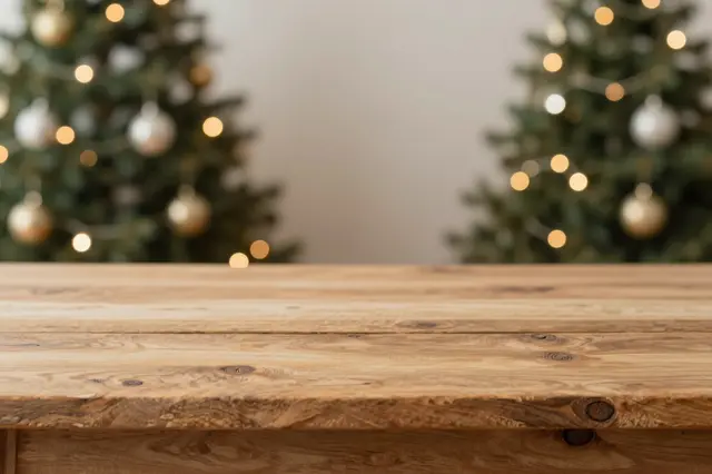 An empty rustic wooden tabletop sits in front of blurred lit Christmas trees with warm bokeh lights