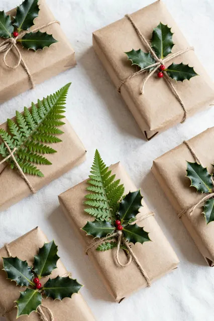 Top view of Christmas gifts wrapped in brown kraft paper decorated with holly, ferns and jute twine arranged on white linen.