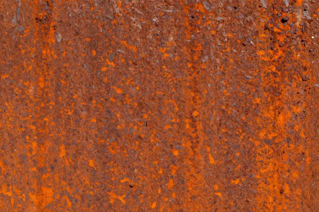 Close-up full frame view of a textured rusted metal surface with bright orange patina and dark corrosion.
