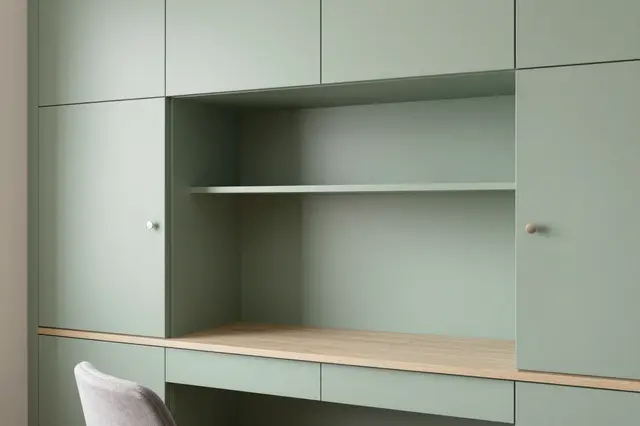 Partial view of a minimalist sage green built-in home office nook with light wood desktop