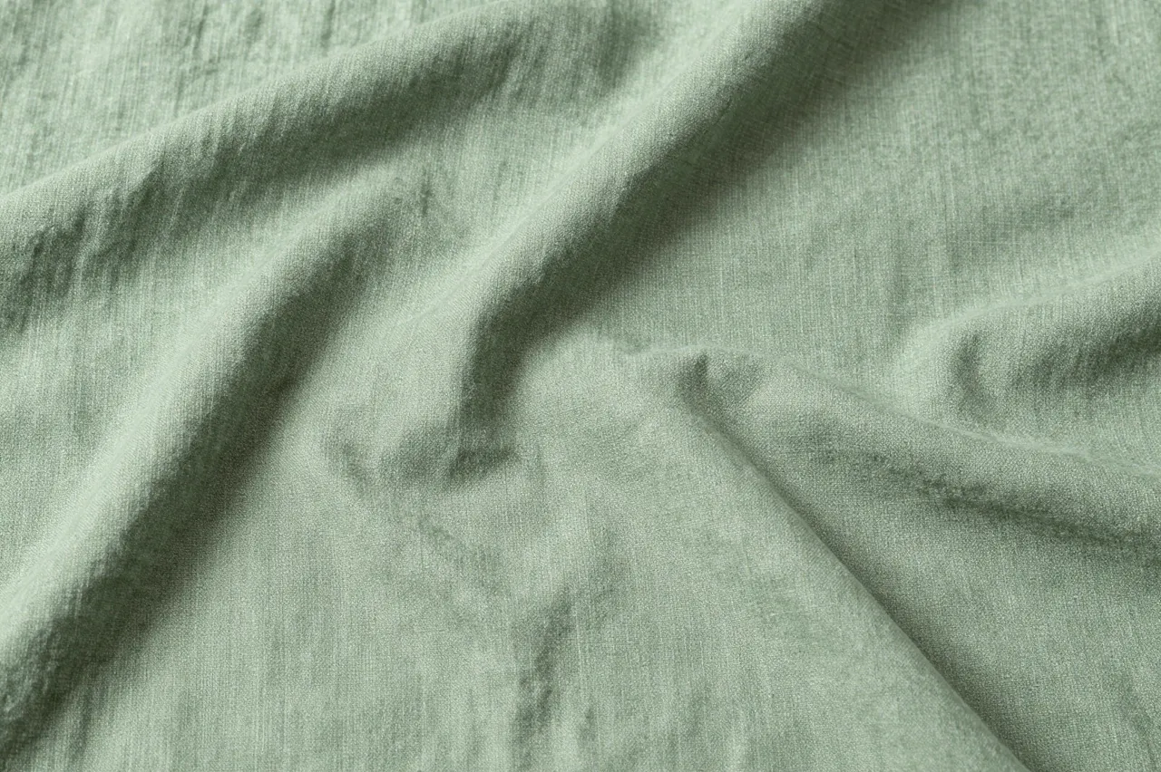 Top view of soft creased sage green linen fabric with natural folds and copy space