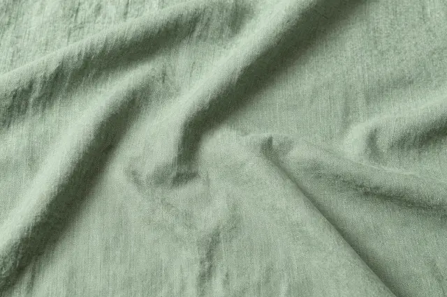 Top view of soft creased sage green linen fabric with natural folds and copy space