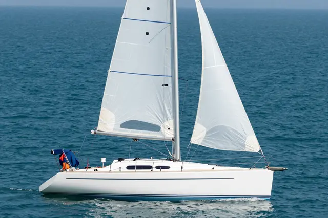A white sailing yacht glides across calm deep blue open water under soft hazy skies.