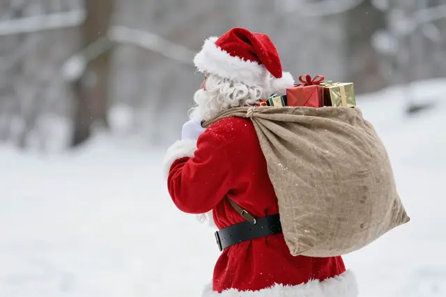 Santa Claus viewed from behind carries a sack of wrapped gifts through falling snow in a winter landscape