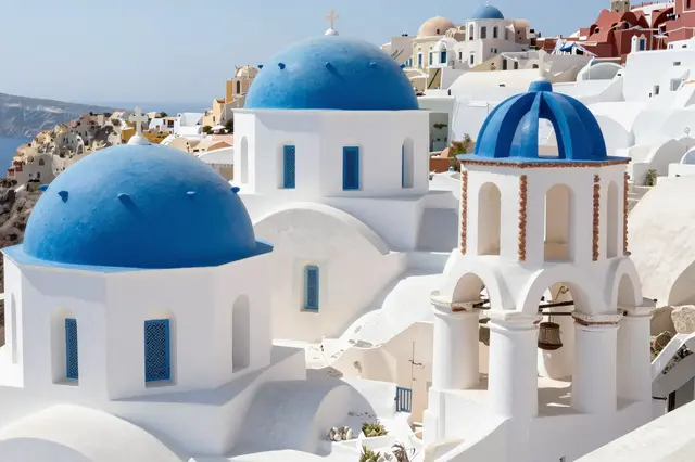 Sunlit whitewashed buildings with bright blue domes overlook the Aegean sea on a Greek island.