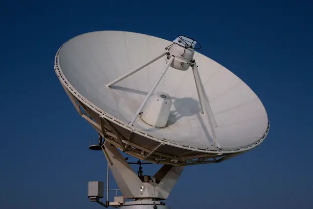 A large white satellite dish stands against a smooth deep dark blue evening sky