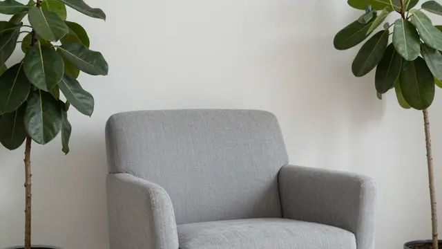 Gray upholstered armchair flanked by two leafy fiddle leaf fig plants against a plain white wall