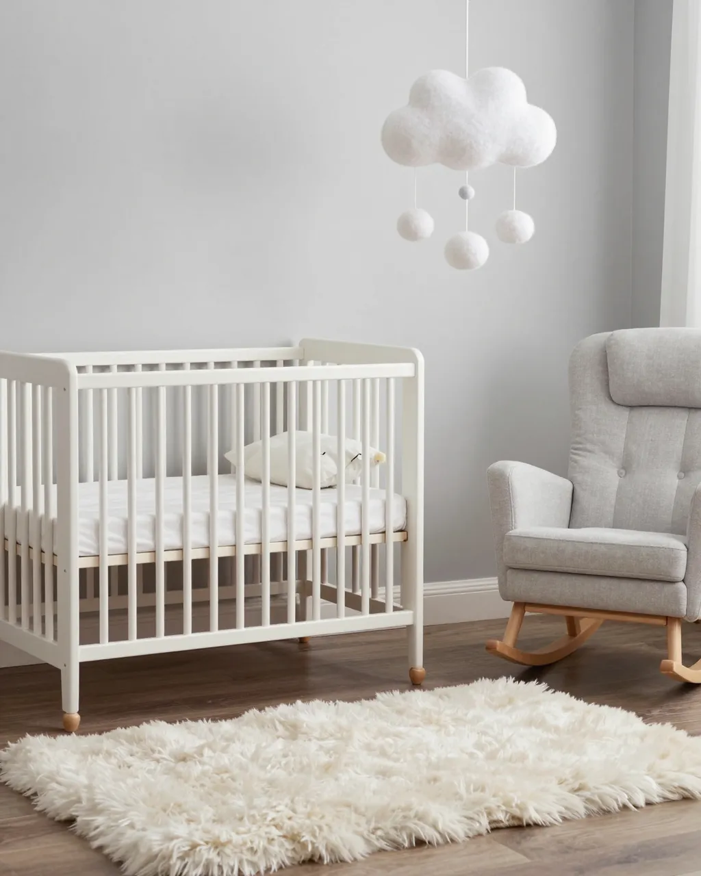 Minimalist scandi nursery with white crib, gray rocking chair, fluffy rug and hanging cloud mobile