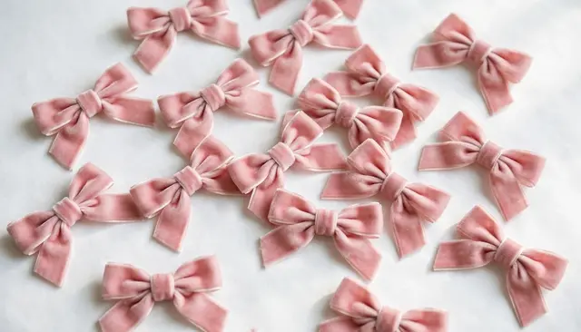 Top view of small dusty pink velvet bows scattered across a plain white surface in soft daylight