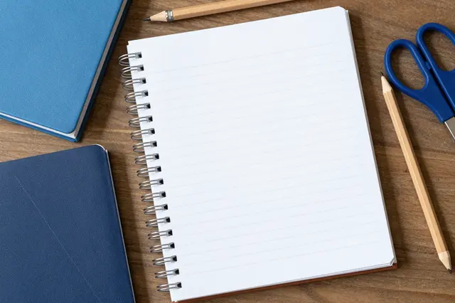 Top view of notebooks, pencils and blue scissors arranged on a wooden table surface