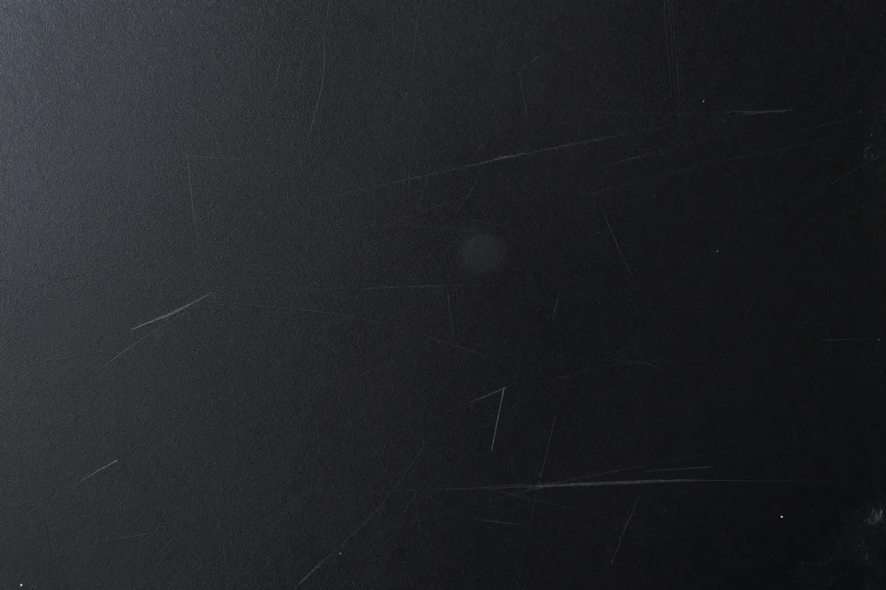 Full frame close-up of a scratched dark black painted metal surface with fine light abrasions