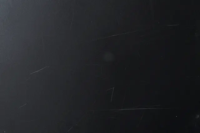 Full frame close-up of a scratched dark black painted metal surface with fine light abrasions