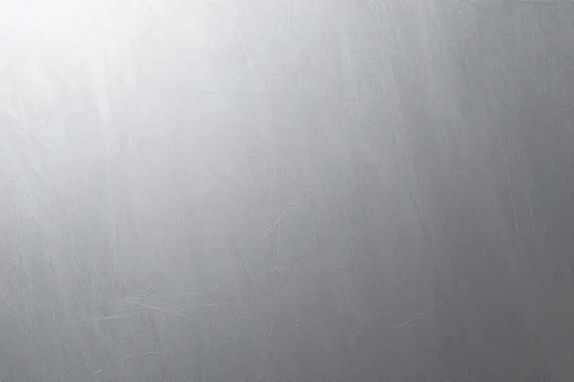Full frame close-up of a gently scratched matte brushed aluminum surface with soft gradient lighting