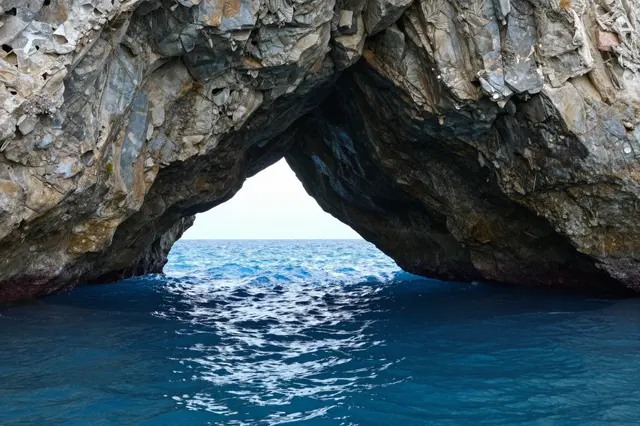 Looking out through a natural rocky sea cave arch onto bright rippling blue ocean water