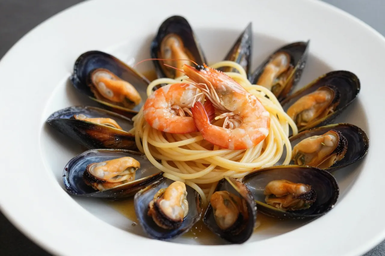 A wide white bowl holds spaghetti topped with cooked shrimp and arranged mussels in a light savory sauce.
