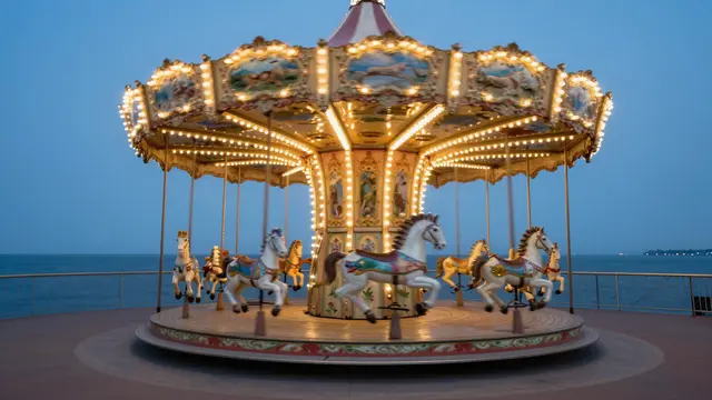 An empty illuminated carousel sits on a seaside promenade during calm blue hour twilight