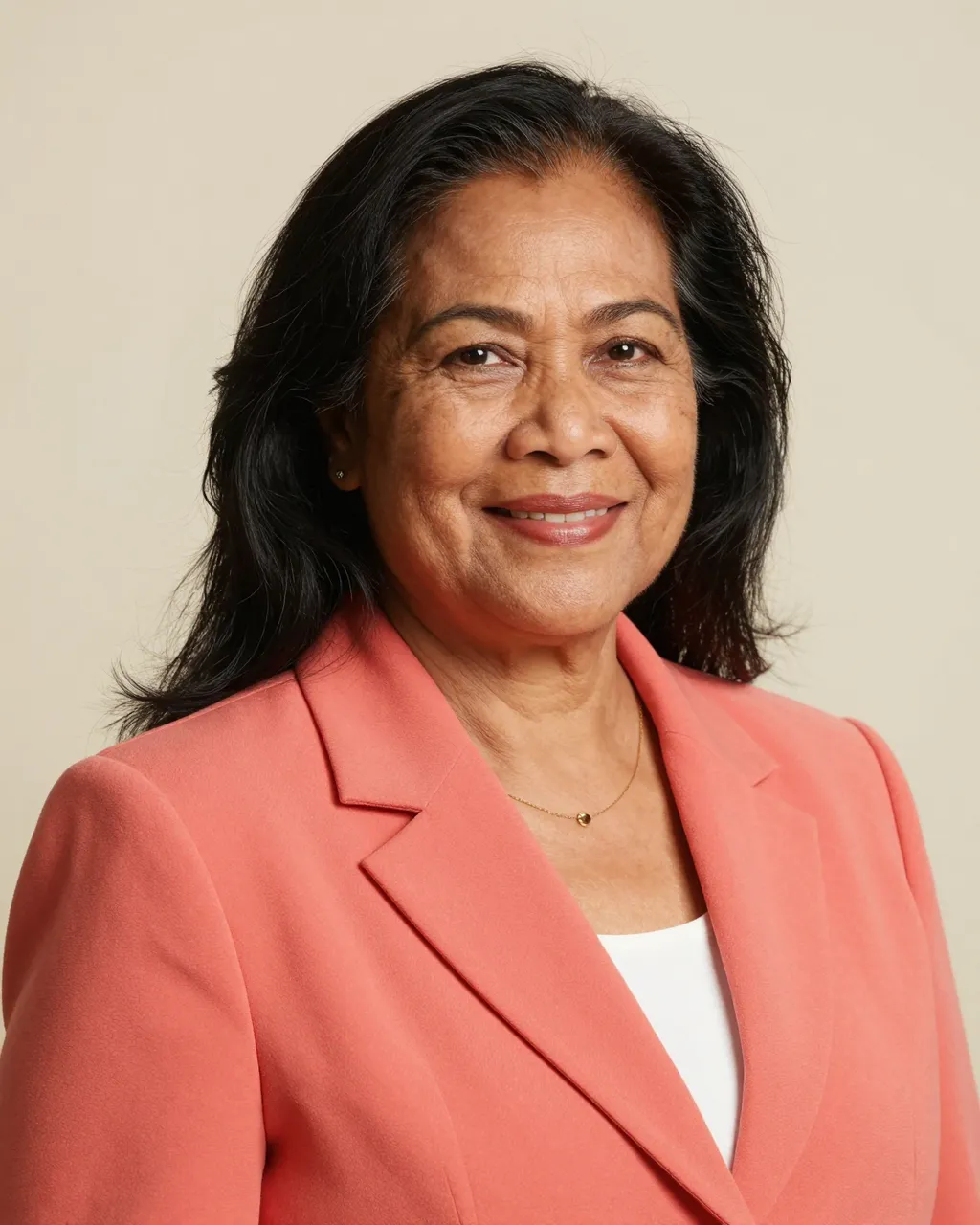 Studio portrait of a smiling senior Pacific Islander woman wearing a coral blazer against a plain cream backdrop
