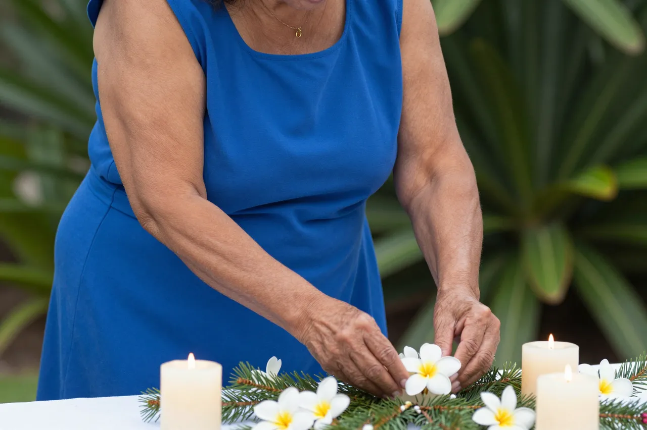 Older Pacific Islander woman in a blue dress arranging frangipani and candles on an outdoor festive table